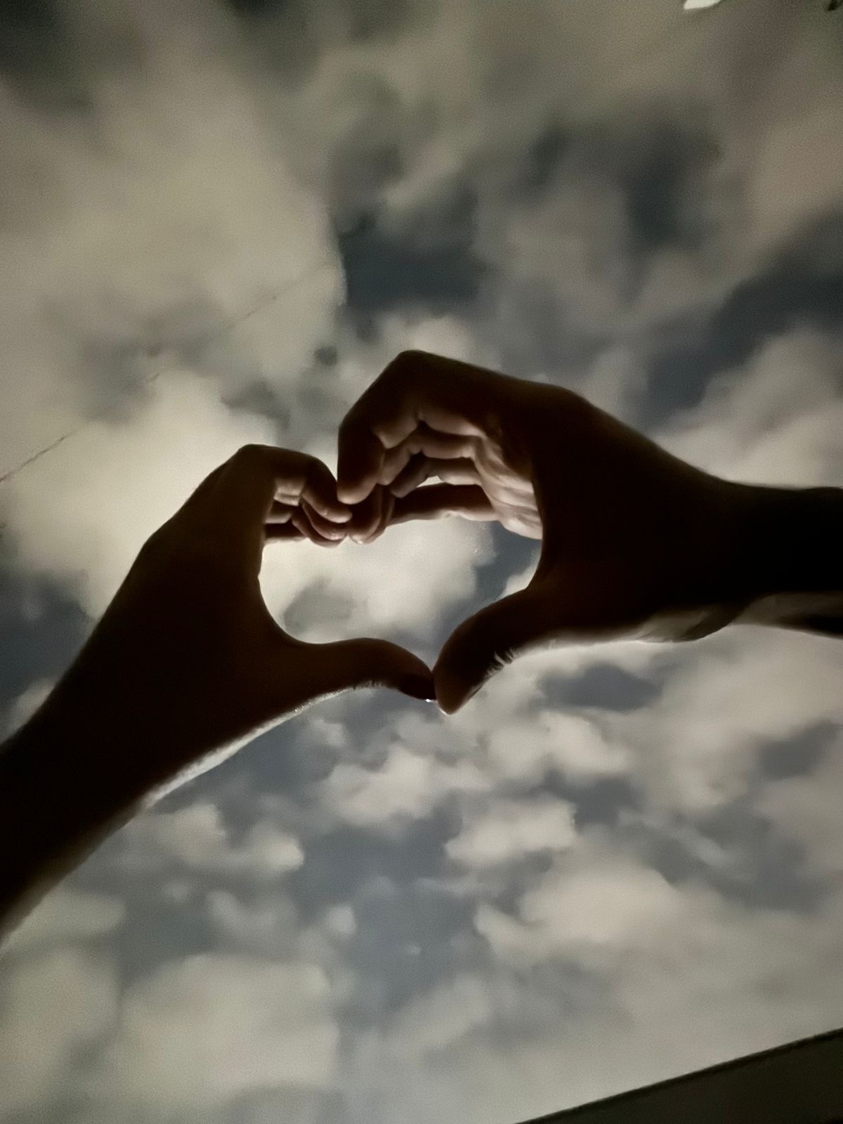 A heart shape made with hands against the sky.